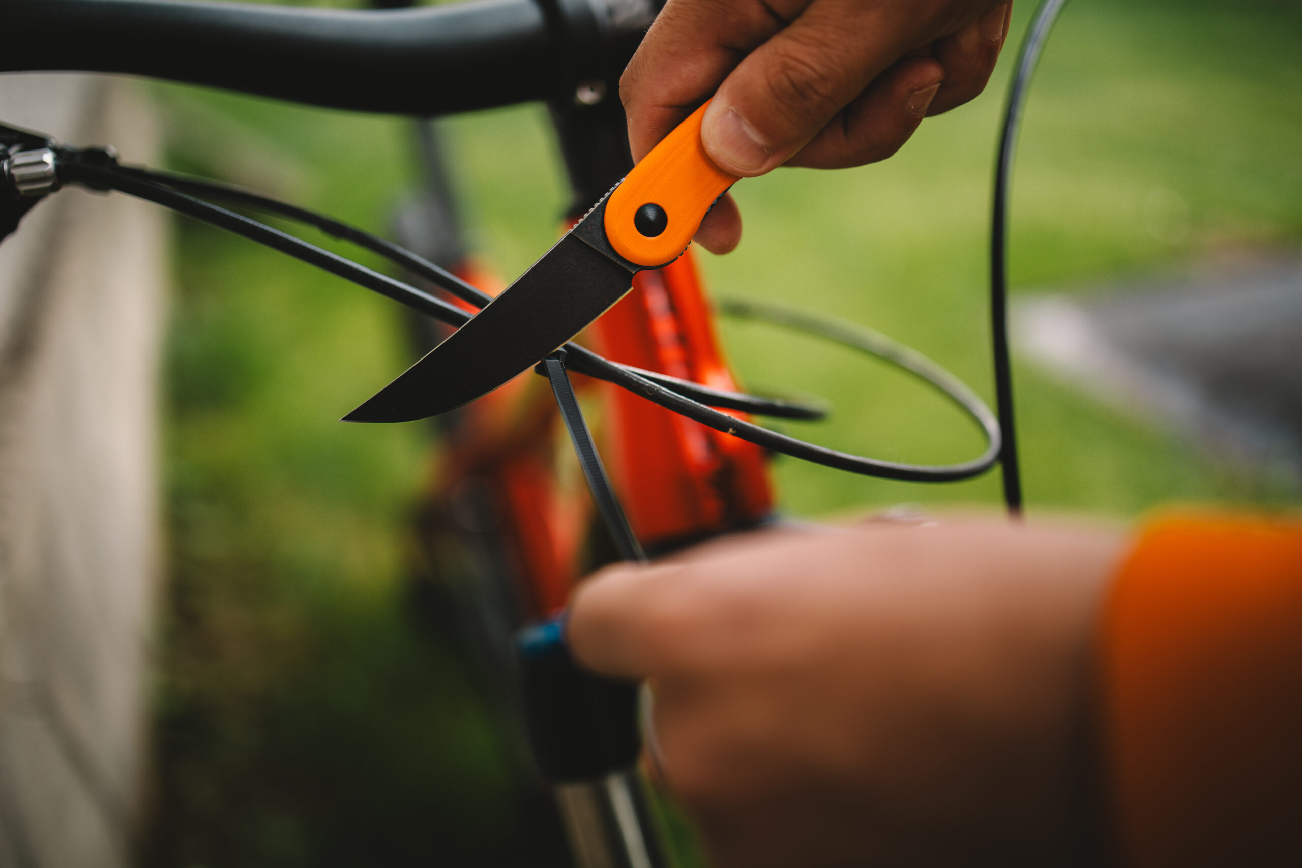 28 Person holding an orange pocket knife near a bicycle outdoors